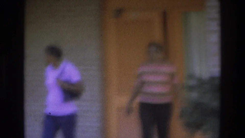 1975 Atlanta home-movie frame with one woman walking past the camera view and another near the orange house door.