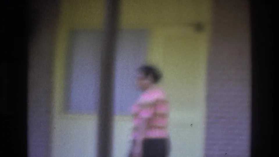 1975 Atlanta 8mm frame showing a striped-shirt pedestrian moving through a sidewalk scene with yellow wall panels.
