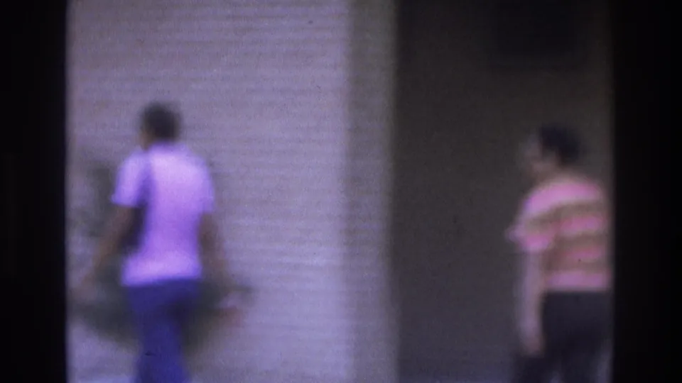 1975 Atlanta 8mm frame with the walking woman near a building wall and a striped-shirt pedestrian at the edge of the sidewalk scene.