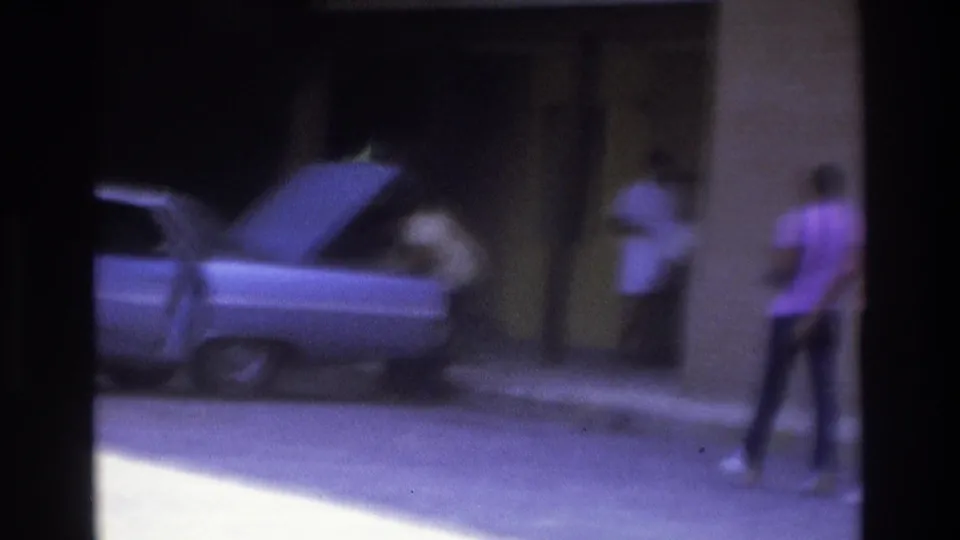 Atlanta 1975 home-movie frame showing a parked car with its trunk open and people near a building entrance.