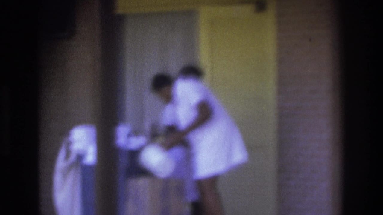 Atlanta 1975 frame of a woman in a white uniform handling items near an exterior doorway.