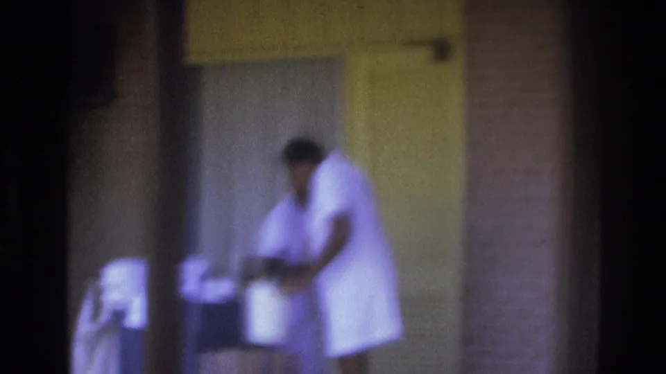 Atlanta 1975 home-movie frame showing a woman in a white uniform working with items near a building entrance.