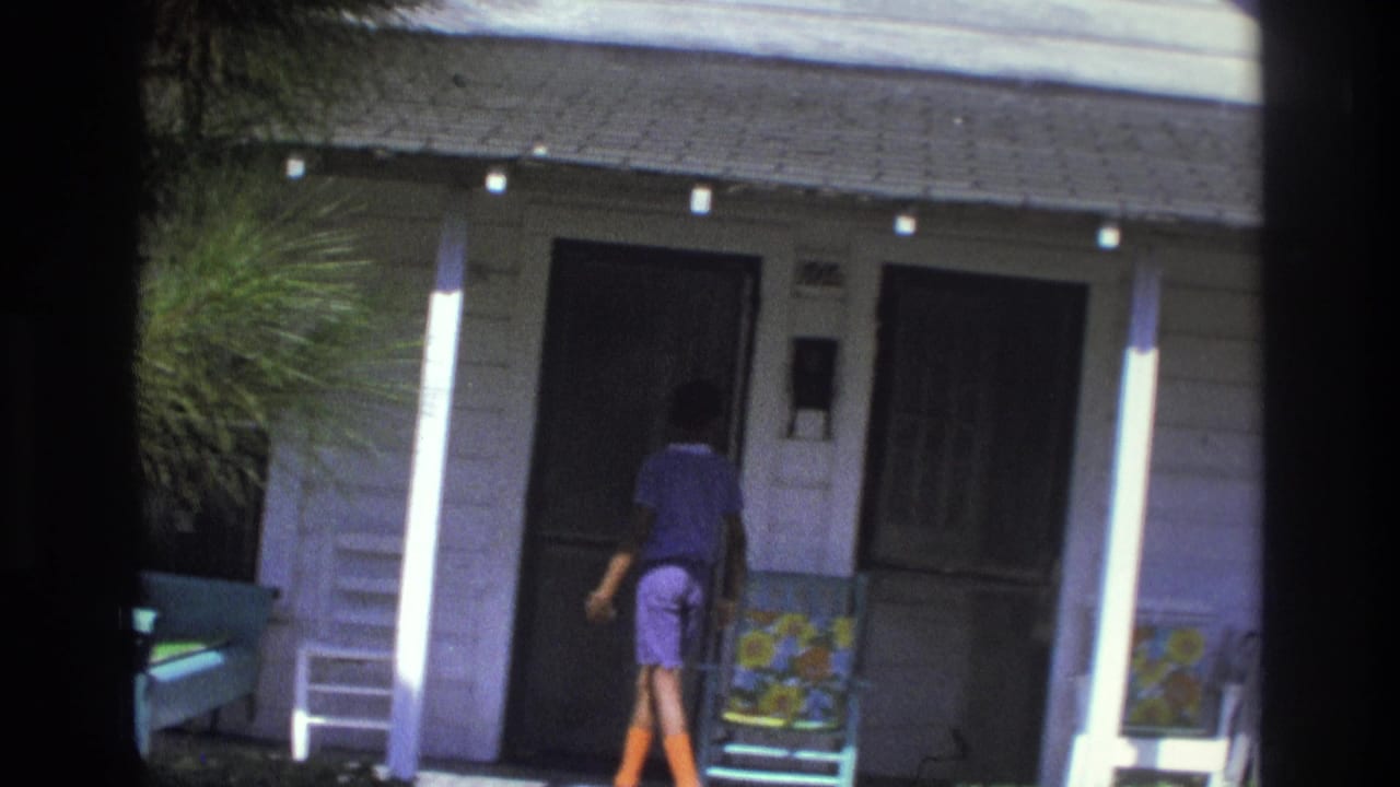 1975 Atlanta home-movie frame showing a person approaching the porch and screen door of a modest white house.