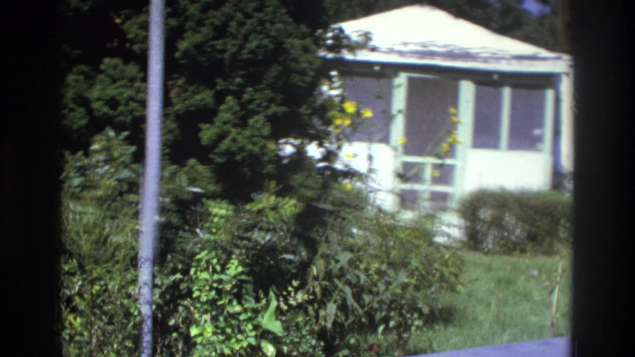 1975 Atlanta frame of a small white residence with screened porch, lawn, shrubs, and bright sun exposure.