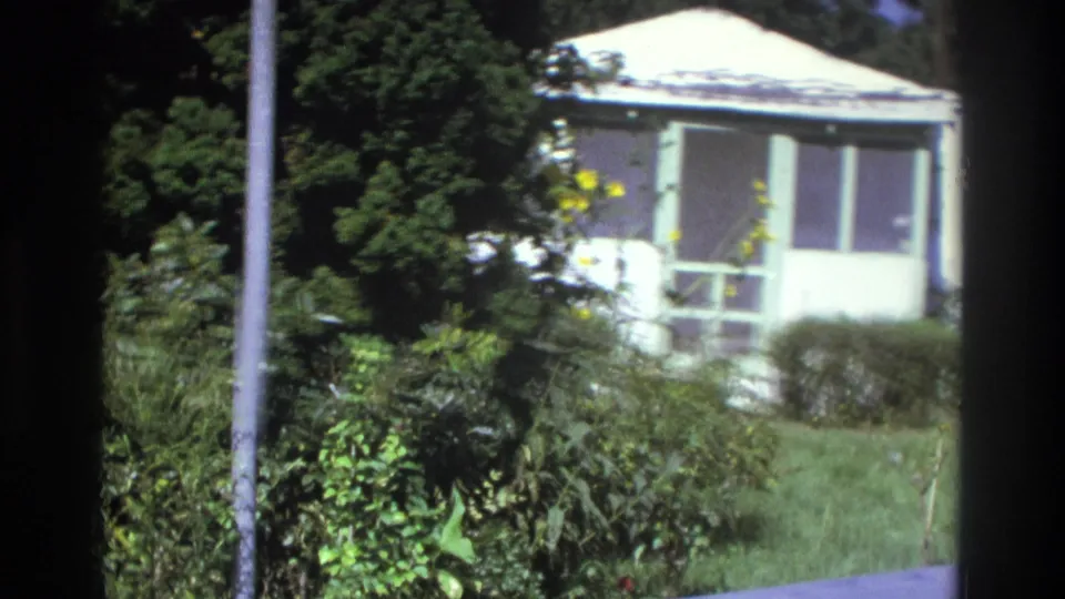 1975 Atlanta frame of a small white residence with screened porch, lawn, shrubs, and bright sun exposure.