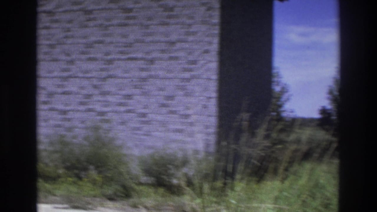 Stone or brick wall beside tall grass and an opening to a distant landscape.