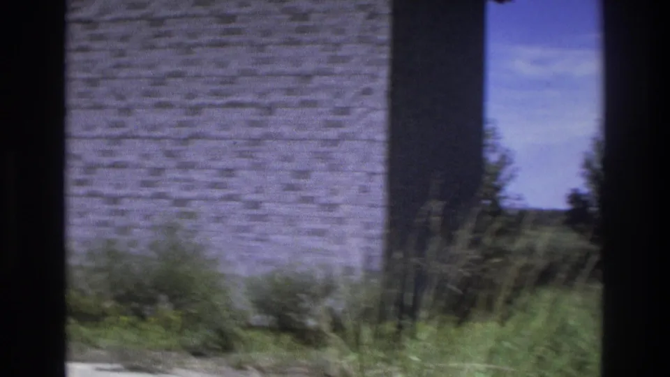 Atlanta-area 8mm frame with a rough masonry wall, tall grass, and a distant outdoor view under blue sky.