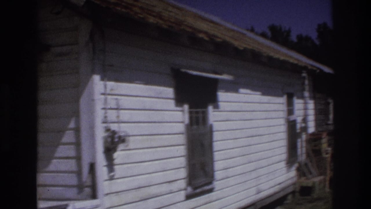 1975 Atlanta-area 8mm frame showing the side of a weathered white clapboard house with a small window and deep shadow.