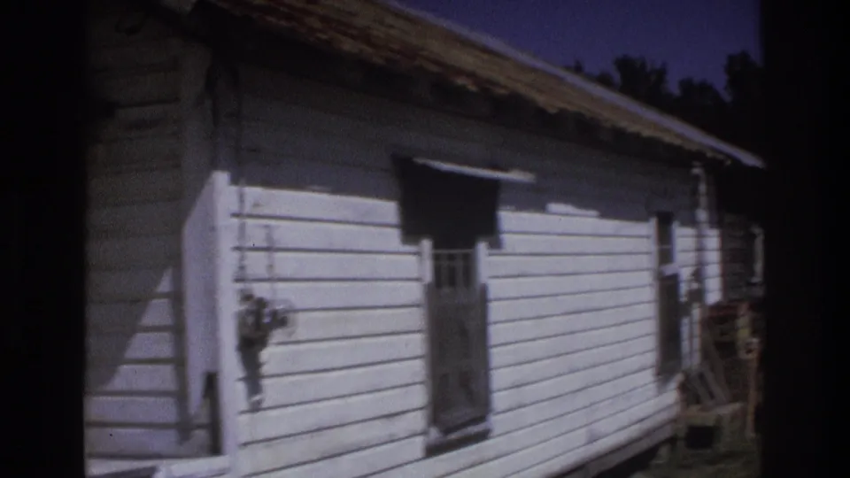 1975 Atlanta-area 8mm frame showing the side of a weathered white clapboard house with a small window and deep shadow.