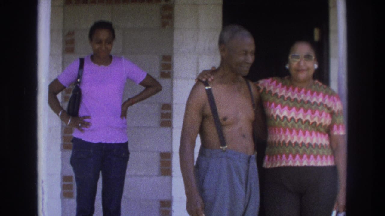 Three adults stand near a doorway in 1975 Atlanta footage, including an older man in suspenders and women in purple and patterned tops.