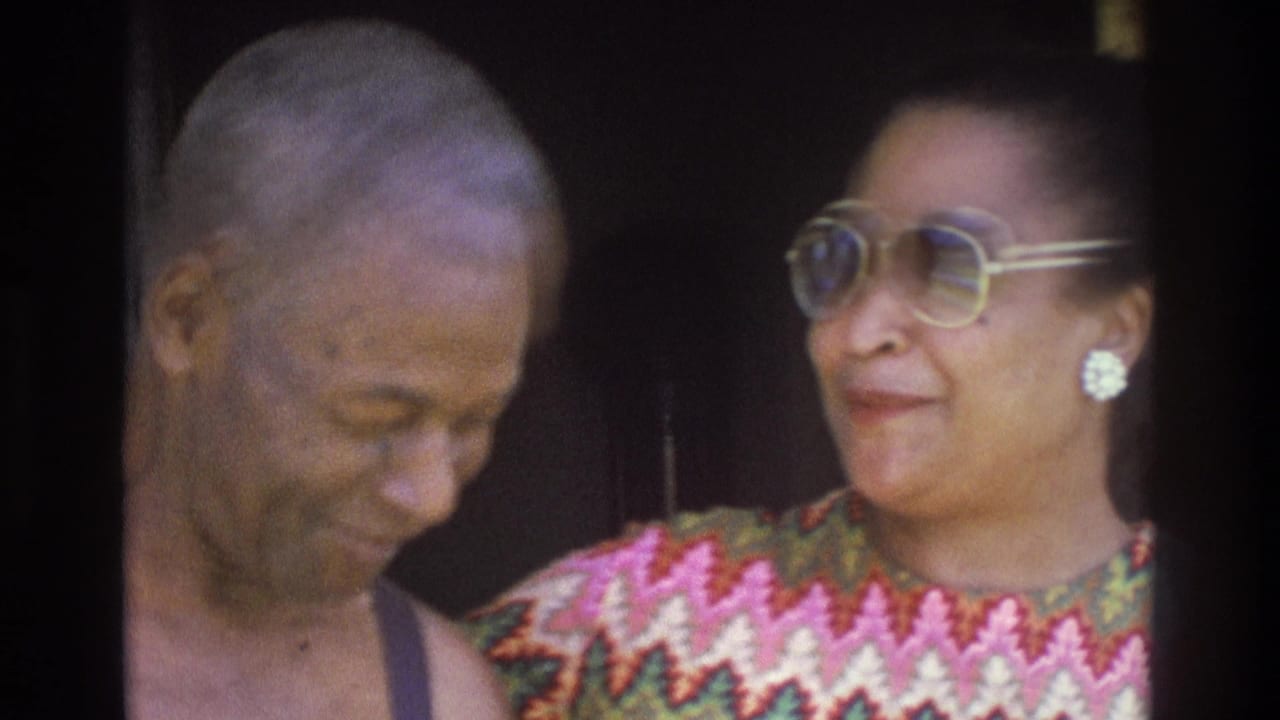 1975 Atlanta home-movie frame showing a shirtless man and a woman in large sunglasses standing close outside a doorway.