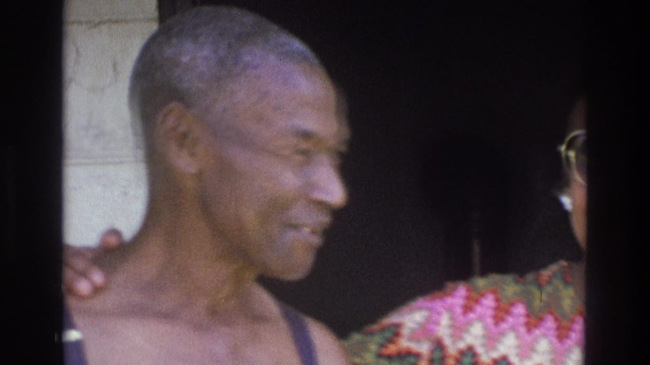 1975 Atlanta home-movie frame with a smiling man in profile beside a woman in a colorful patterned dress and sunglasses.