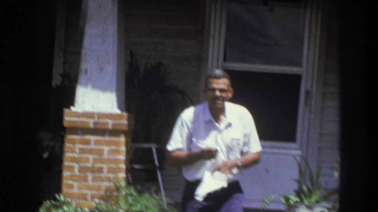 In 1975 Atlanta home-movie footage, an adult man in a white shirt stands on a porch while holding a white towel.