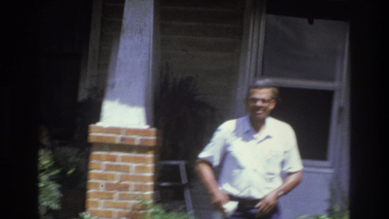 Adult man smiles on the porch while holding a white towel at his waist.