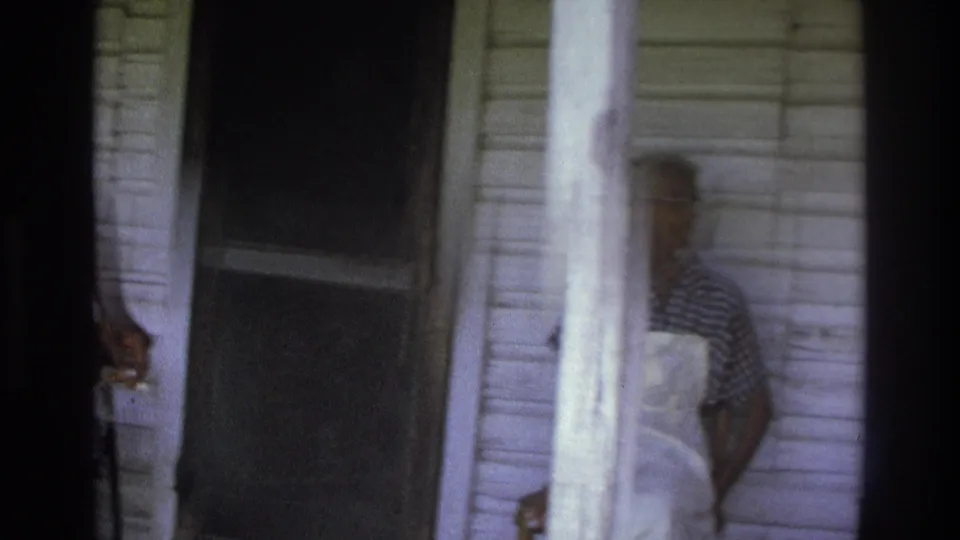 A porch view in the 1975 Atlanta clip shows white siding, dark vertical film framing, a screen door, and a partially visible adult near the edge.
