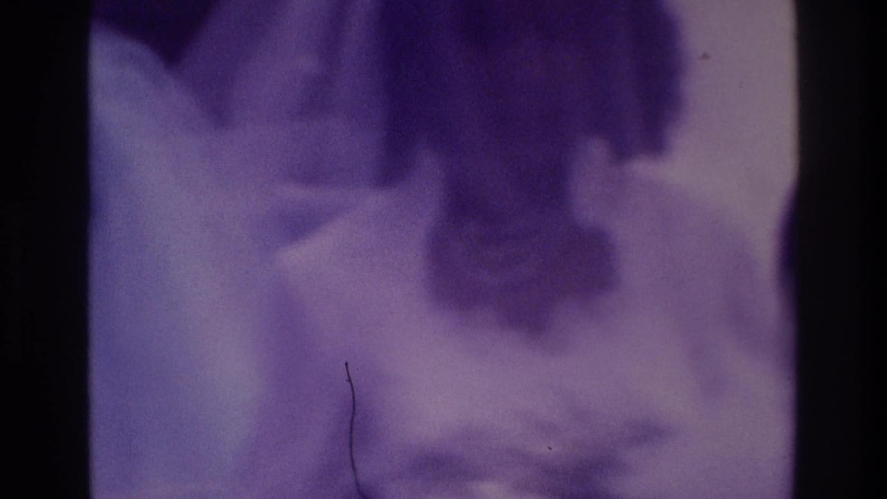 Soft-focused bride and groom with nearby guests in a purple-tinted wedding home-movie frame.