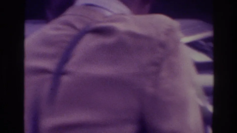Atlanta 1975 wedding home-movie frame with a close, soft view of light formal fabric and a partially visible person near the ceremony area.