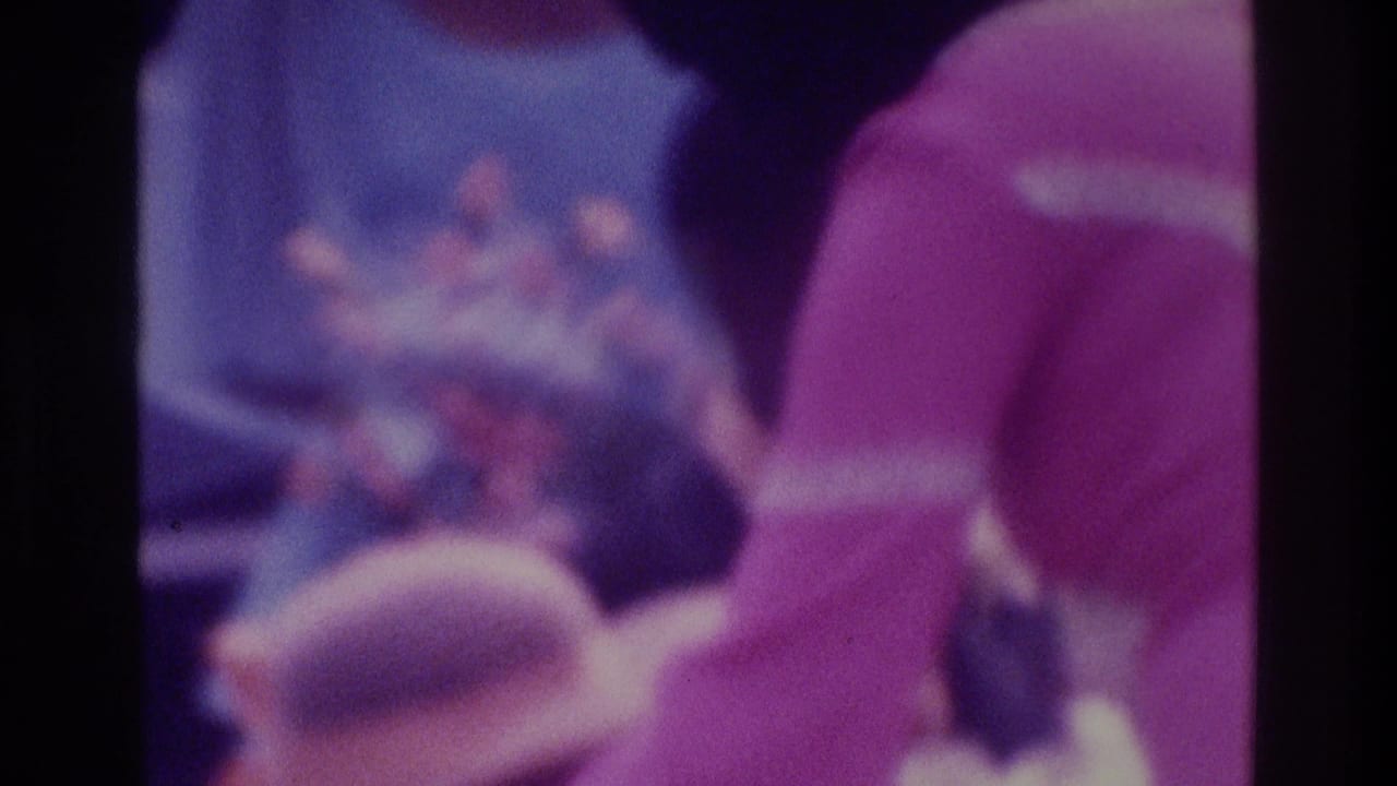 Soft 1975 Atlanta home-movie frame showing wedding guests gathered near the bride, with purple color shift and dark film borders.