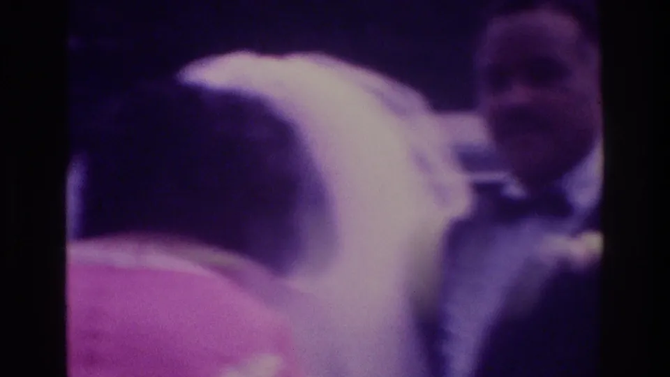 Soft 8mm frame from a 1975 Atlanta wedding showing the bride in veil beside the groom in tuxedo, surrounded by guests.