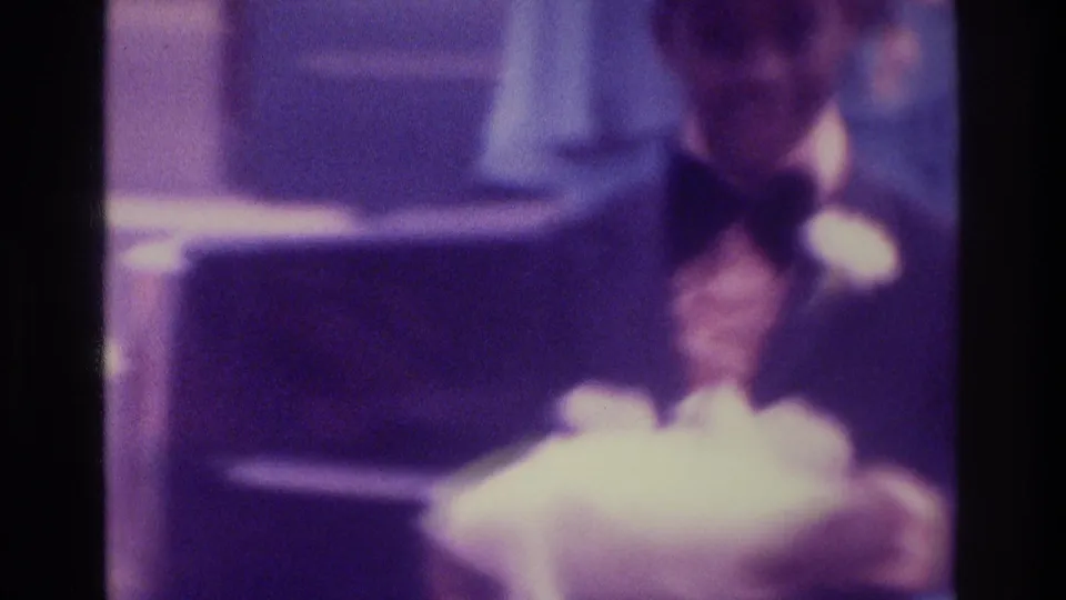 Soft 1975 Atlanta wedding frame showing the groom in tuxedo holding white fabric, likely part of bridal attire or accessories.