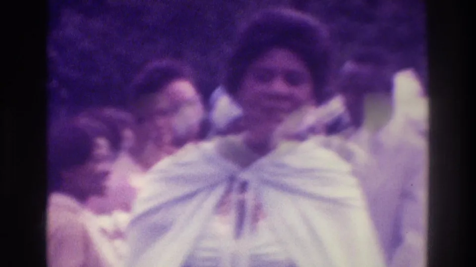 A woman in a white shawl stands among wedding guests outdoors in the 1975 Atlanta home-movie scene.