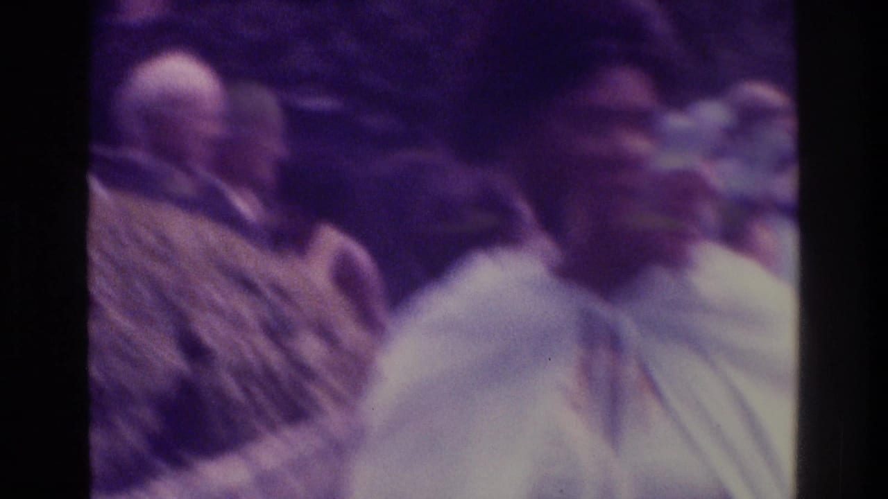 Soft 8mm frame from 1975 Atlanta showing adults in a crowded outdoor social setting, including a man in patterned clothing and blurred faces.