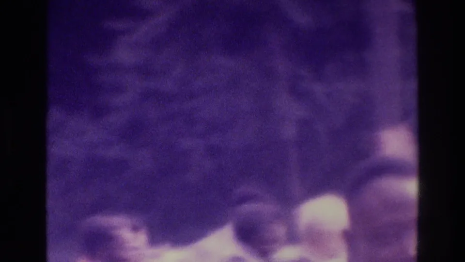 Shaky 8mm frame from the 1975 Atlanta crowd clip, with indistinct adults passing close to camera and strong purple film coloration.