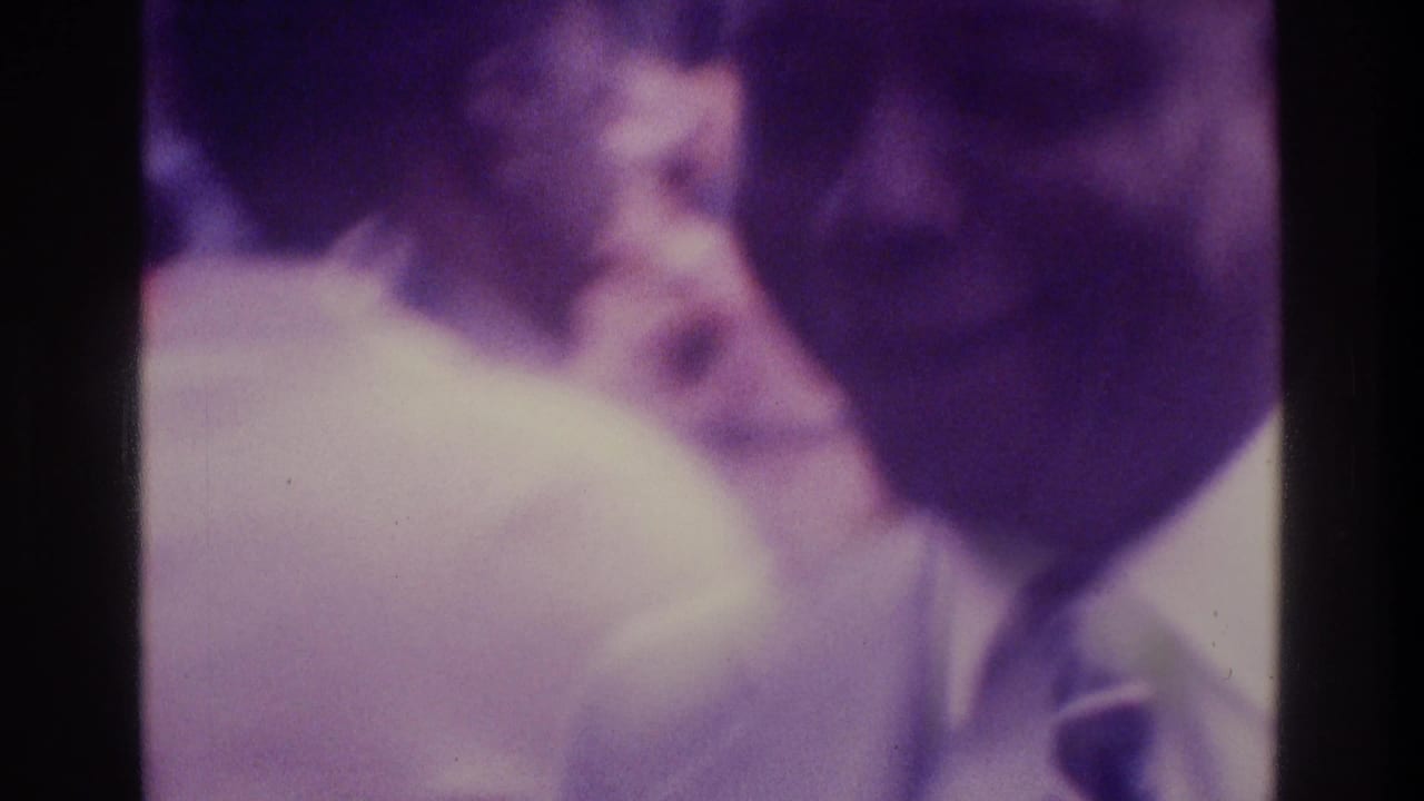 Blurred view of people standing close together, with a suited man at the right edge.