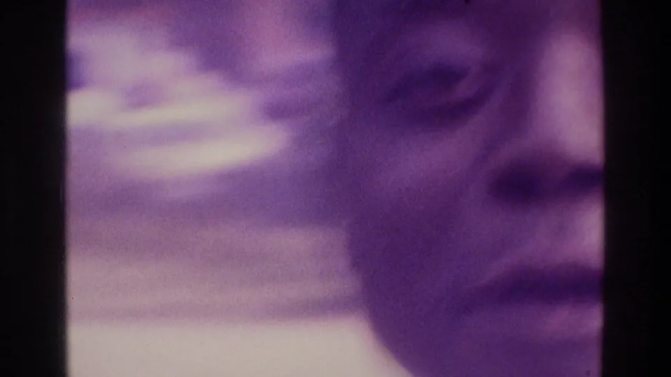 Soft, purple-tinted close-up from the 1975 Atlanta home movie, showing a man's face partially framed by overexposed film light.