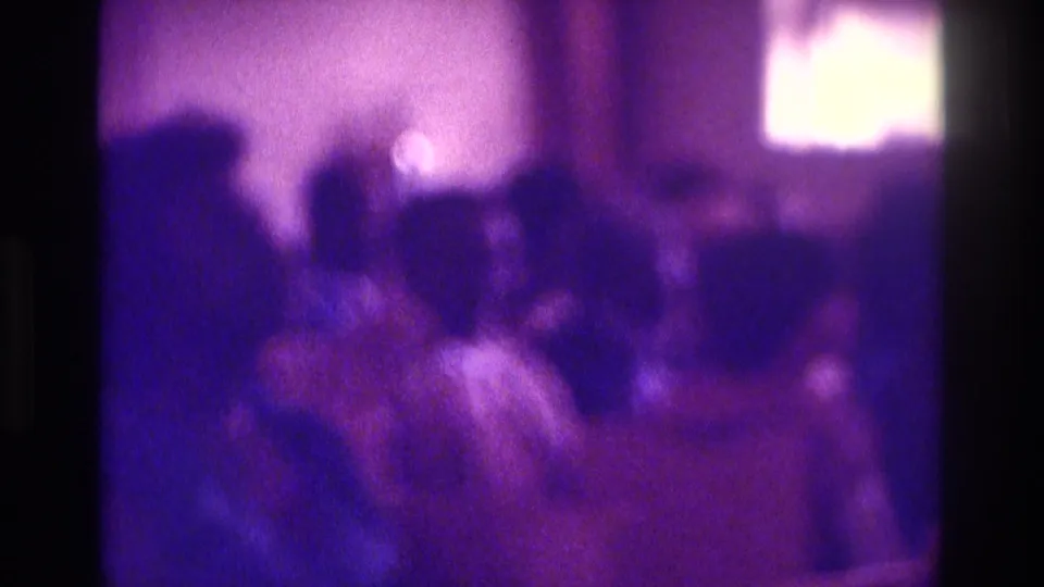 Soft, grainy 8mm frame from a 1975 Atlanta church interior, with congregants blurred by motion and low light.