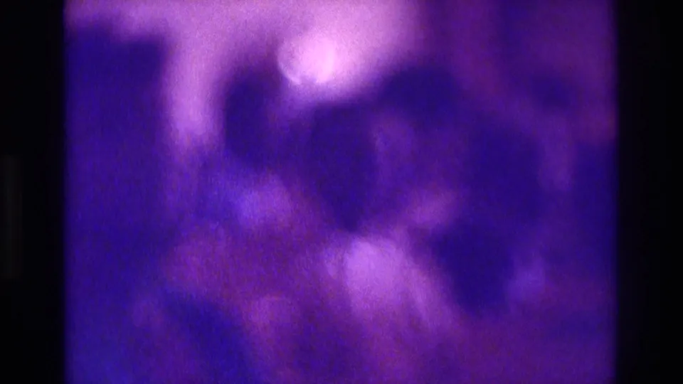 Low-light 1975 Atlanta church-service frame with indistinct seated figures and heavy purple 8mm color shift.