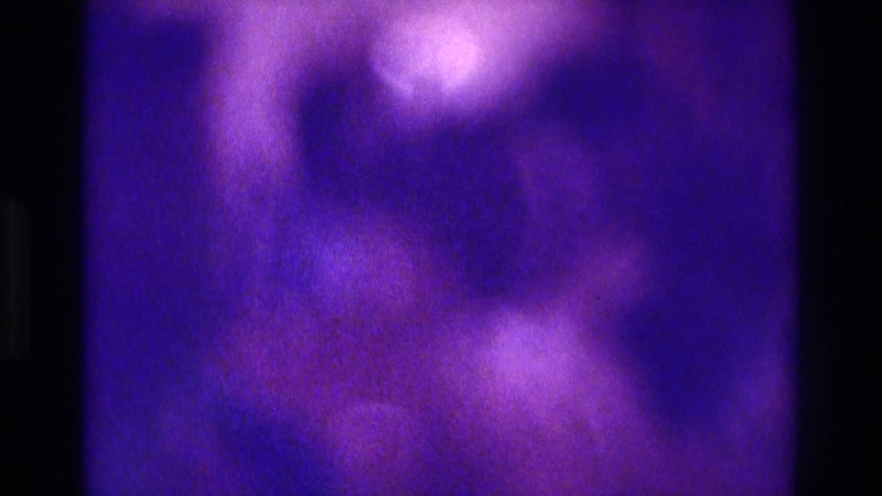 Soft, purple-tinted 8mm frame from the 1975 Atlanta home-movie clip, showing an indistinct dim interior with no clear figures.
