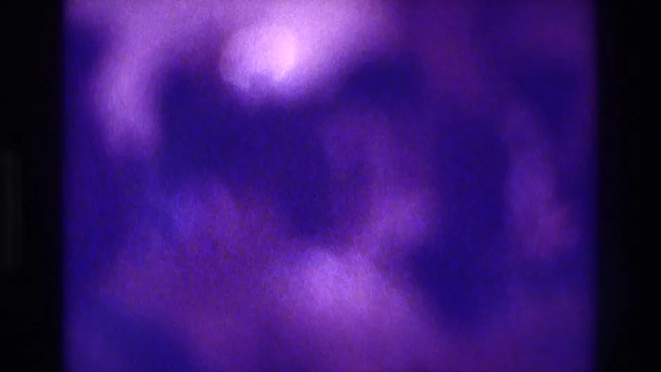 Purple-tinted 8mm party frame with blurred light areas and indistinct interior forms, consistent with low-light home-movie footage.