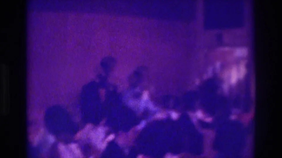 1975 Atlanta home-movie party frame showing several silhouetted people in a dim interior under heavy purple-blue tint and grain.