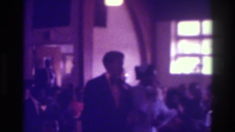 1975 Atlanta wedding frame with the couple near the foreground, seated guests, and bright windows behind them.