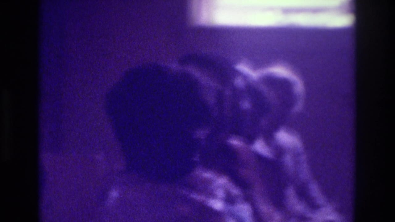 Soft, grainy view of people grouped together under purple light.