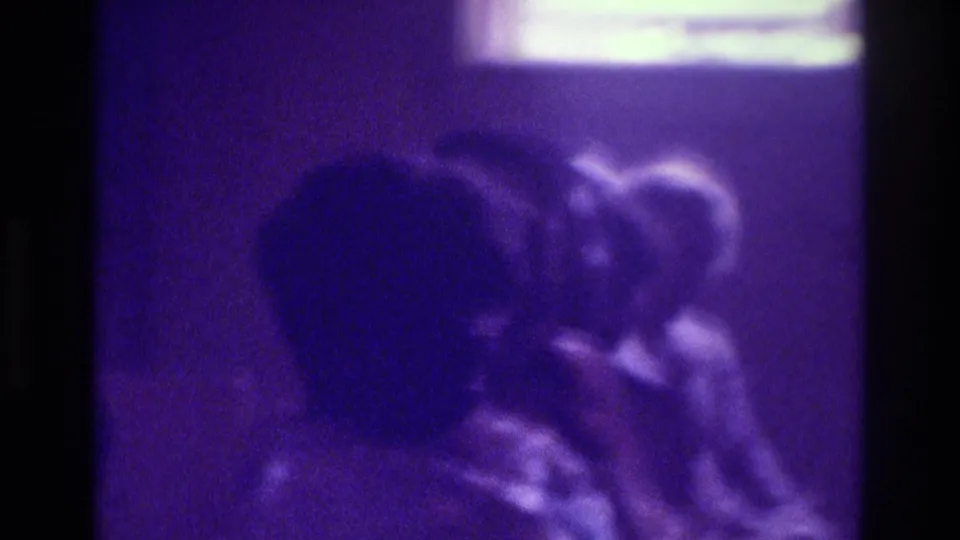 Purple-tinted 8mm frame from Atlanta in 1975 showing blurred seated figures with a pale light source at the top edge.