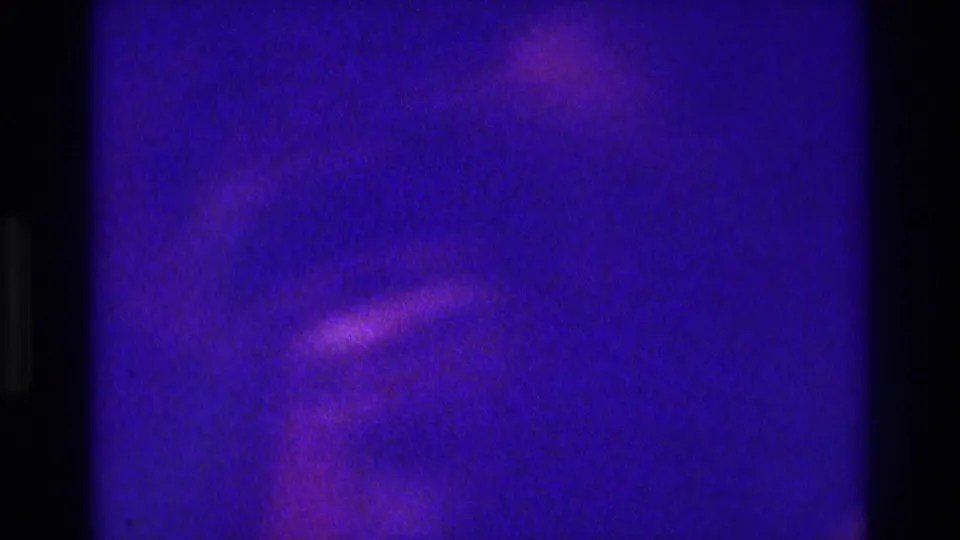 Dark 1975 Atlanta 8mm frame with an indistinct face or figure emerging from purple-blue grain and low interior light.