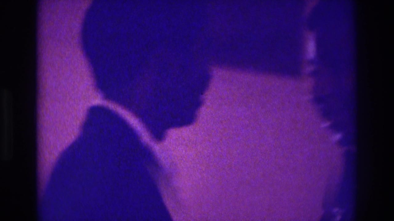 A suited man in profile faces another person at the edge of the frame.