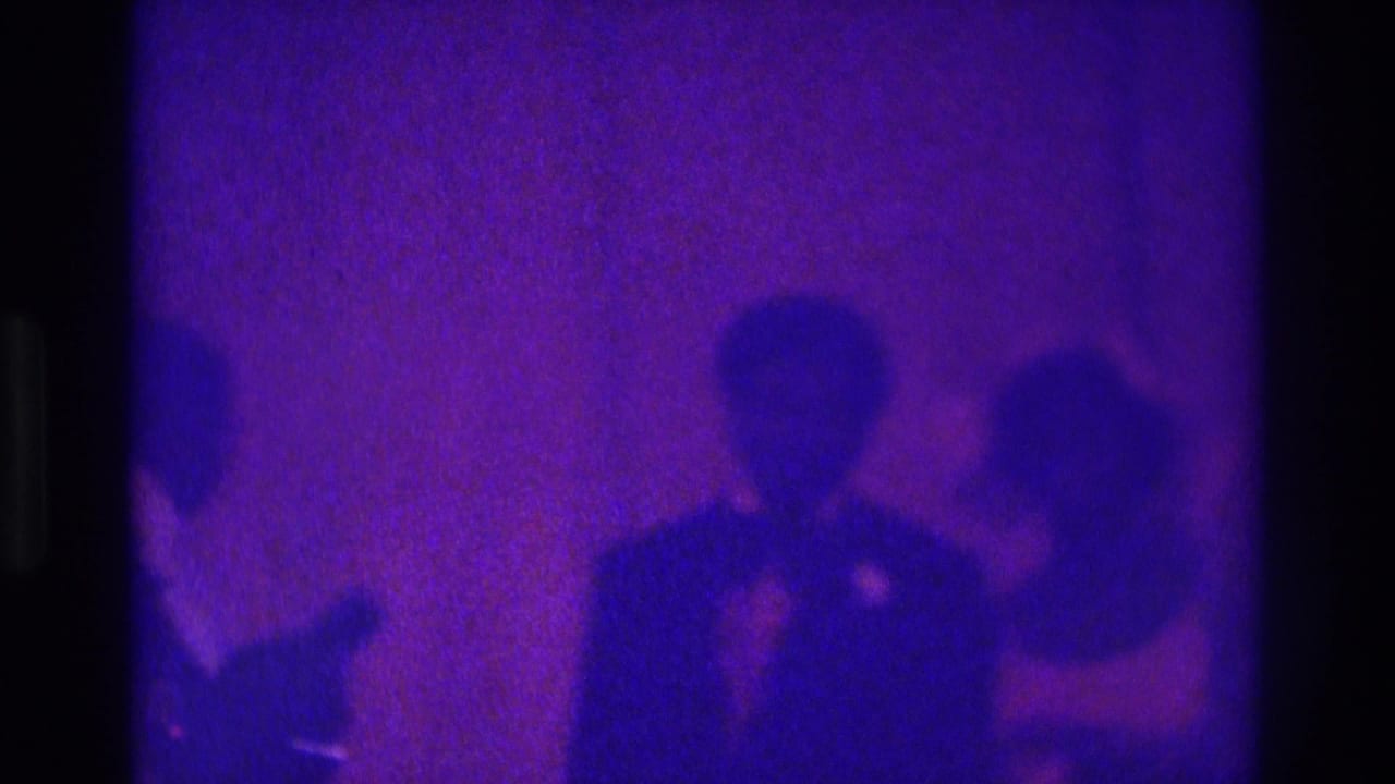 1975 Atlanta 8mm frame showing a bridal couple and guests standing in a dim room under strong purple-blue color shift.