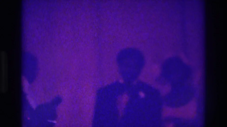 1975 Atlanta 8mm frame showing a bridal couple and guests standing in a dim room under strong purple-blue color shift.