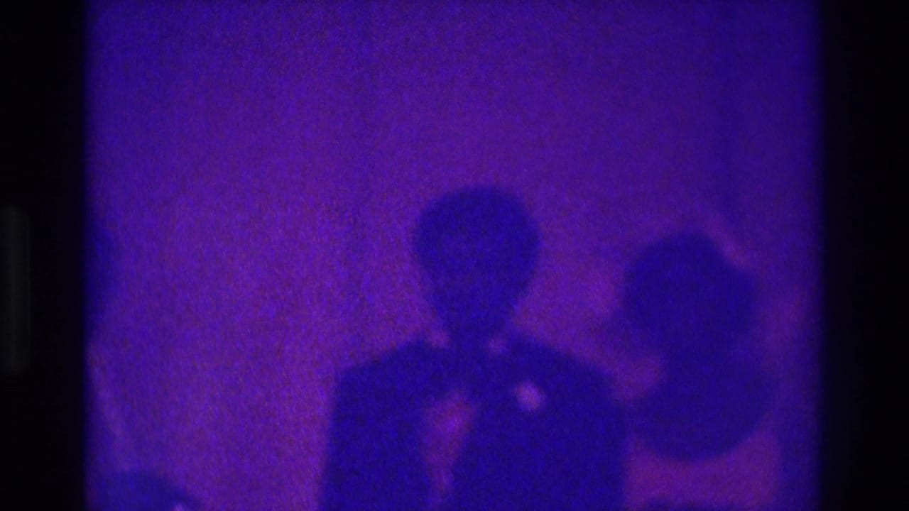 Soft 8mm frame from Atlanta in 1975 with the couple centered and guests at the margins in low purple light.
