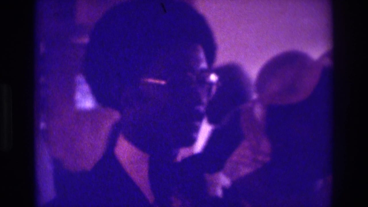 1975 Atlanta 8mm frame showing a man in glasses and dark suit in profile beside a woman in white during a wedding ceremony.