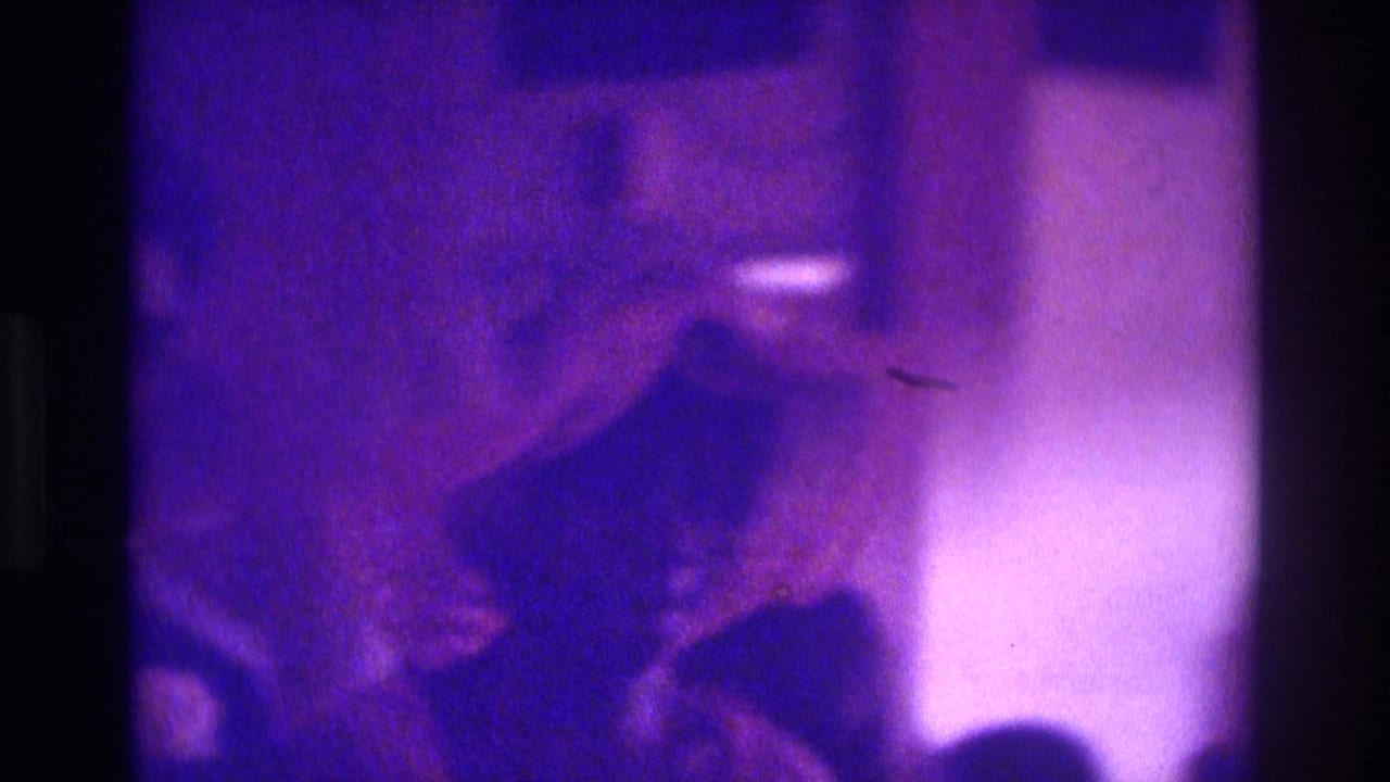 1975 Atlanta 8mm wedding footage showing a dark-suited attendant moving through a dim, purple-cast ceremony interior.