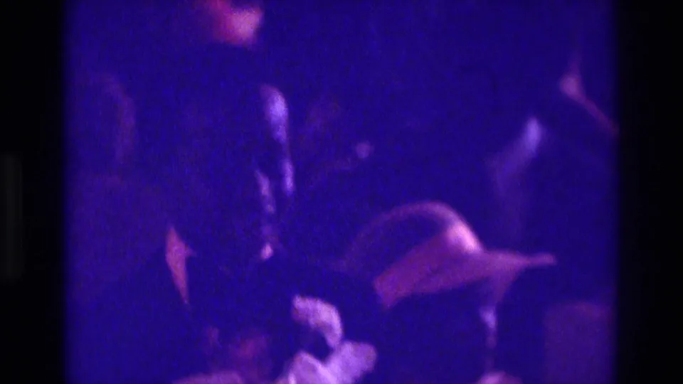 A purple-cast 1975 Atlanta 8mm frame shows wedding party members moving down the aisle among seated guests.