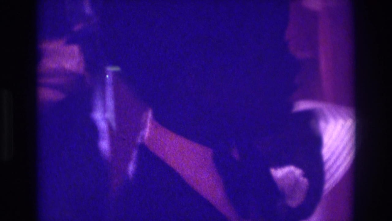 1975 Atlanta 8mm wedding reception frame showing a veiled bride and formal guests in low purple indoor light.