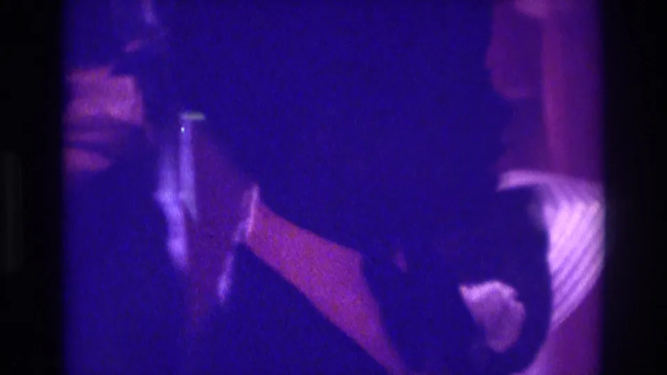 1975 Atlanta 8mm wedding reception frame showing a veiled bride and formal guests in low purple indoor light.