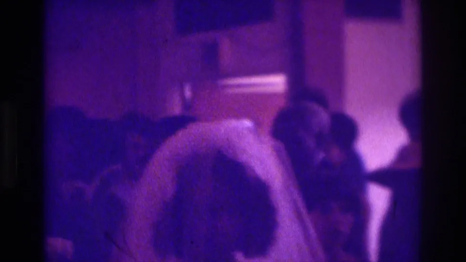 1975 Atlanta 8mm frame showing a veiled bride near a tuxedoed man in a low-light wedding reception interior.