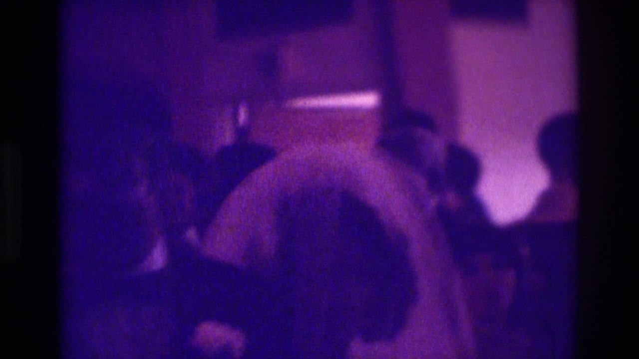 1975 Atlanta home-movie frame showing newlyweds dancing closely indoors as guests stand around them.