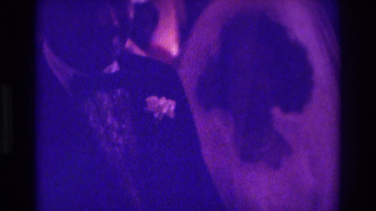Bride and groom seen close together while dancing under purple-tinted light.
